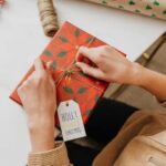 Person Tying a Gold Ribbon on Red and Green Box