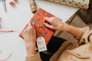 Person Tying a Gold Ribbon on Red and Green Box