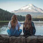 women sitting on rock near body of water