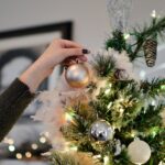 person putting bauble on top of Christmas tree